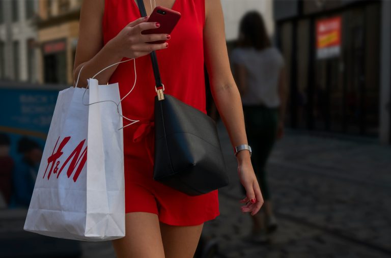 A lady with phone on her hand and a shopping bag hanging on her other hand